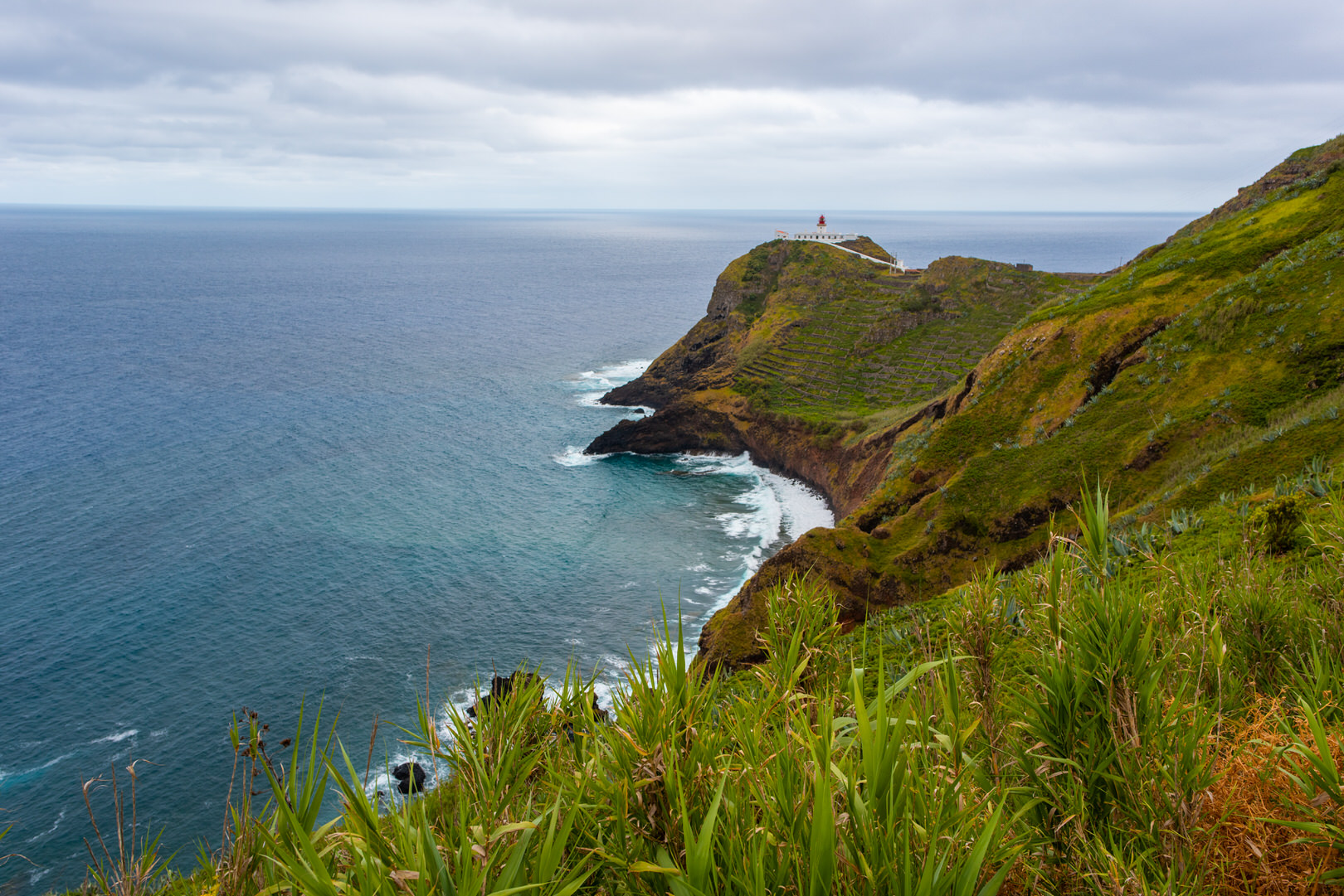 Grüne Felder auf der Azoreninsel Santa Maria und im Hintergrund der Leuchtturm von Maia